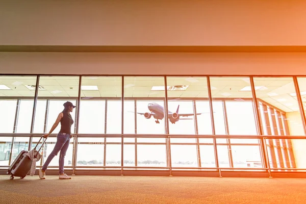 Traveler woman plan and backpack see the airplane at the airport glass window, girl tourist hold bag and waiting near luggage in hall airplane departure. Travel Concept .