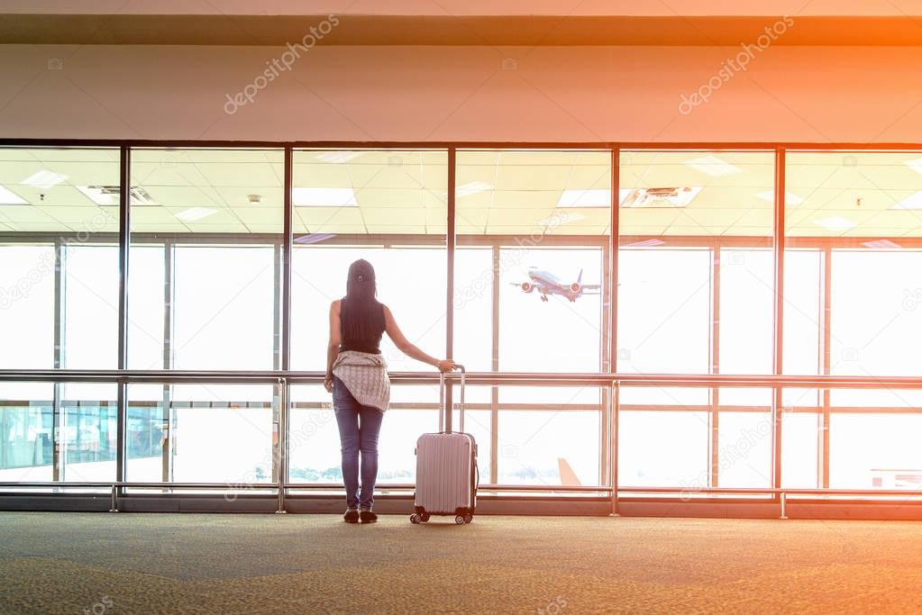 Traveler woman plan and backpack see the airplane at the airport glass window, girl tourist hold bag and waiting near luggage in hall airplane departure. Travel Concept .