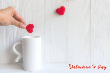 Beyaz fincan kahve, eski ahşap arka plan kırmızı kalp tutan el. Sevgililer kavramı