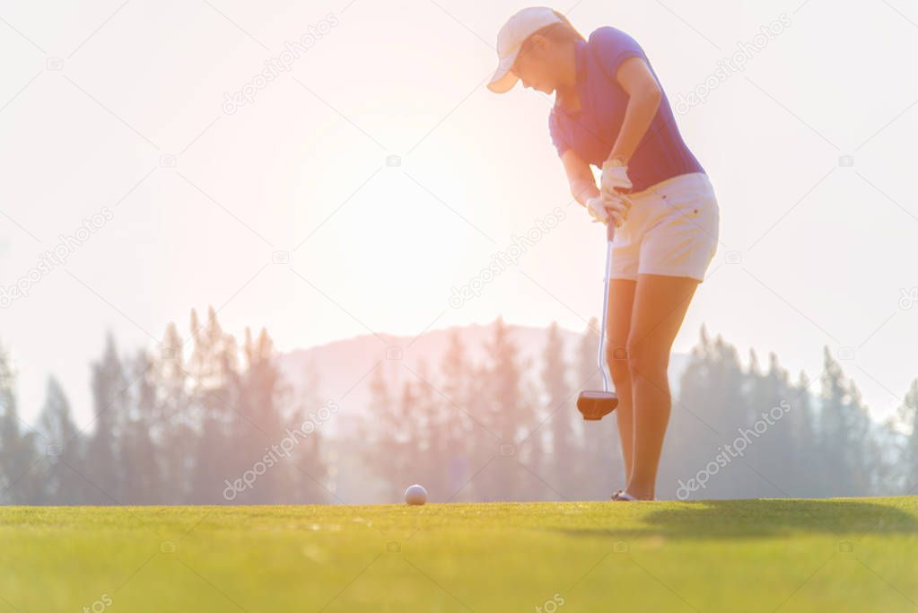 Golfer asian woman putting golf ball on the green golf on sun set evening time.  Healthy and Lifestyle Concept.