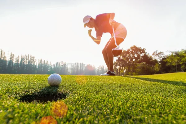 Asyalı kadın golfçü eylem sonra yeşil golf, günbatımı zamanı, kopya alanı uzun koyarak golf topu kazanmak için. Sağlıklı kavramı