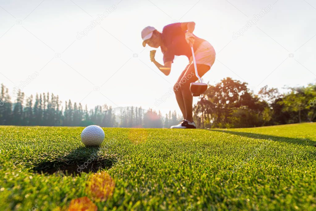 Asian woman golfer action to win after long putting golf ball on the green golf, sunset time, copy space.  Healthy Concept