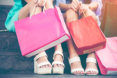 Alışveriş merkezinde alışveriş sonra merdivende alışveriş çantası ile oturan iki genç kadın. Yaşam tarzı kavramı. Vintage sesi