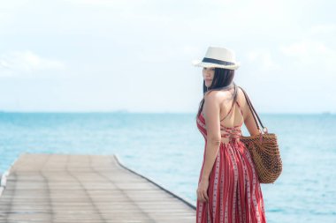 Yaz günü. Kadın gülümsüyor rahatla ve kırmızı giyen elbise moda ayakta ahşap Köprü'de deniz, mavi gökyüzü arka plan. Seyahat ve tatil. Özgürlük kavramı