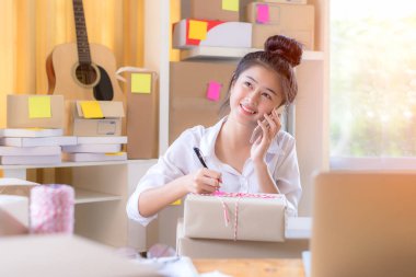 Asya genç kadın paket ürün hazırlamak için müşteriden online sipariş yazılı gülümseyen. Evde çalışmak için yaşam tarzı.  