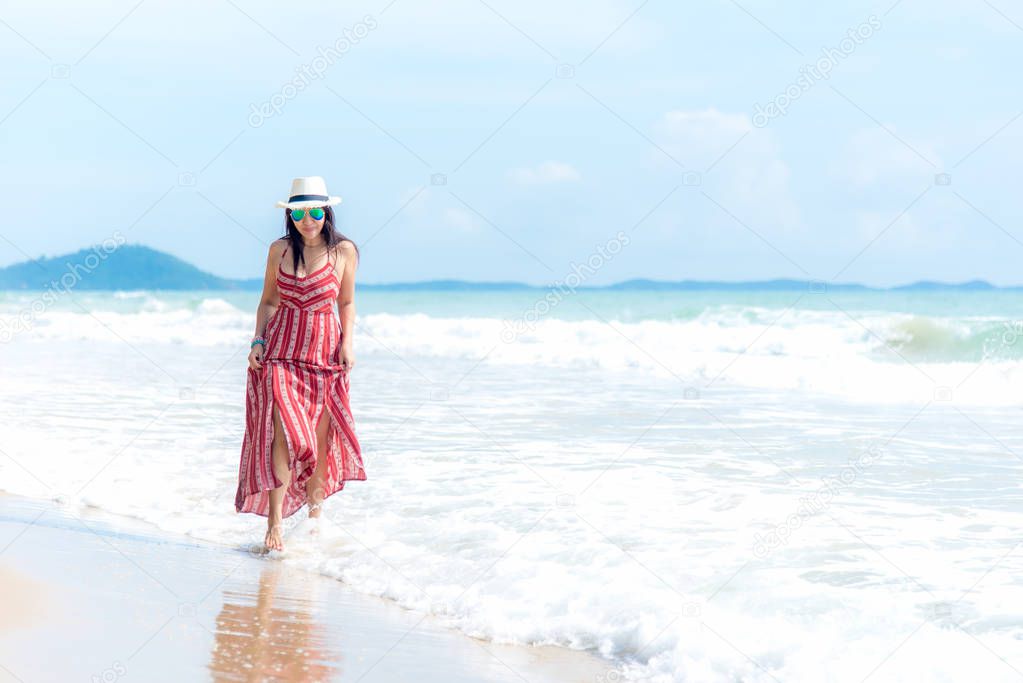 Summer Day. Smiling woman wearing fashion summer walking on the sandy ocean beach. Happy woman enjoy and relax vacation. Lifestyle and Travel Concept