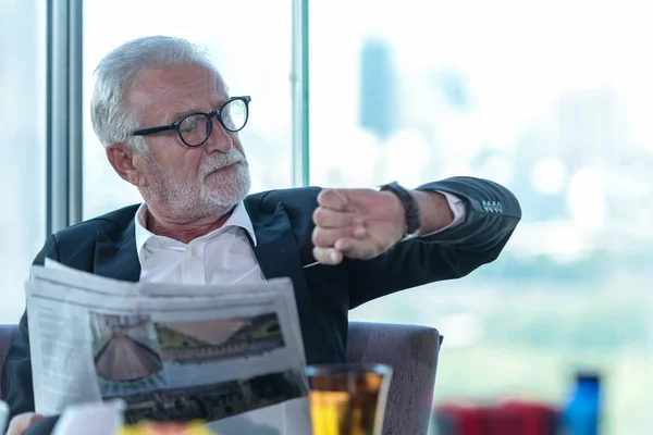 Portrait business partner executive smart man sitting and reading newspaper in restaurant. Old people businessman see the time and waiting your partner for meeting and taking about work.  Business Concept