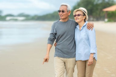 Lifestyle asian senior couple happy walking and relax on the beach.  Tourism elderly family travel leisure and activity after retirement in vacations and summer. clipart