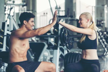Gülümseyen bir çift, spor salonunda halterle egzersiz yaptıktan sonra vücut bakımı ve zayıflığı için beşlik çakıyor. Fitness eğitmeni, spor yapıyor. Diyet ve Sağlıklı Spor Konsepti