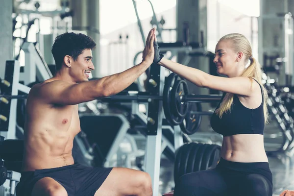 Gülümseyen bir çift, spor salonunda halterle egzersiz yaptıktan sonra vücut bakımı ve zayıflığı için beşlik çakıyor. Fitness eğitmeni, spor yapıyor. Diyet ve Sağlıklı Spor Konsepti