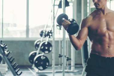 Vücut geliştirici adam spor salonunda dambıl ile egzersiz yapıyor. Sağlıklı bakım ve vücut geliştirme için. Fitness eğitmeni, spor yapıyor. Diyet ve Sağlıklı Spor Konsepti