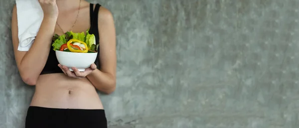 Lifestyle women hold fresh salad after exercise  at the gym workout for healthy care and body slim.  Fitness instructor exercising the fitness. Diet and Healthy sport Concep