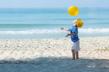 Asyalı küçük kız eğleniyor ve kumsalda sarı top oynuyor. Aile turizmi yaz ve tatil için tatil ve tatil için tatil ve gezinin keyfini çıkarır. Seyahat ve Aile Konsepti