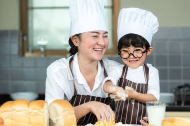 Yemek pişiren aile. Şef anne ve çocuk tost pişiriyor ve akşam yemeği için ekmek yapıyorlar. Asyalı oğul anneye tatlı yemek yapmada yardım ediyor, çok mutlu ve keyifli. Aile Yaşam Tarzı Konsepti
