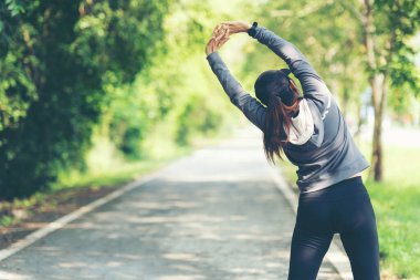 Sağlıklı bir kadın koşmadan önce ısınıyor ve kollarını uzatıp dışarı bakıyor. Asyalı koşucular spor salonu, doğa parkı geçmişi. Sağlıklı ve Yaşam Tarzı Konsepti.
