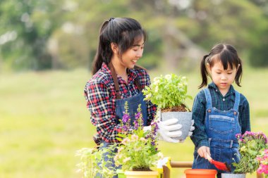 Aile kızı, annesinin bahçeye çiçek dikmesine yardım ediyor. Gençler anne ve kızı bahçeyle uğraşıyorlar. Güneşli doğa geçmişi. Bahar ve yaz günlerinde mutlu ve keyifli. Aile Kavramı
