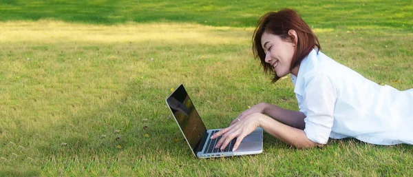 Lifestyle people freelance work from home with laptop on the grass in nature park outdoors.  Young Woman stay home and resting in summer vacations.  copy space and banner for text