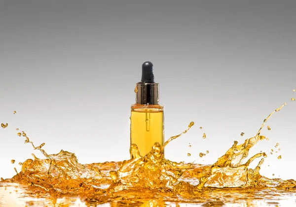 De fles van de gele cosmetische in de grote sinaasappelolie splash — Stockfoto