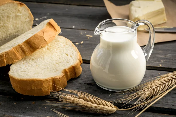 Jarro de leite com pão branco acabado de assar e espigas de trigo — Fotografia de Stock