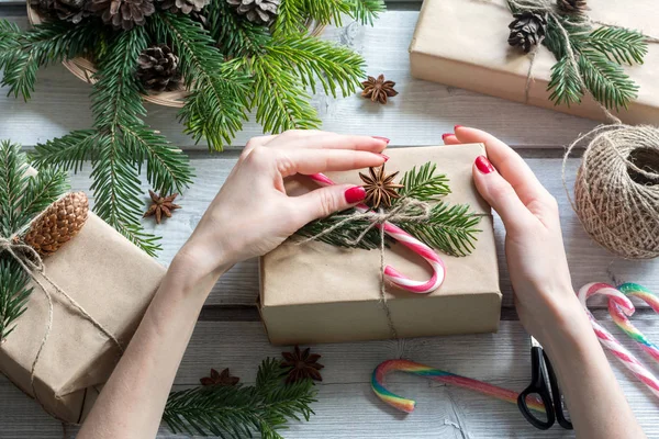 A női kéz díszítő ajándék doboz cukorkát nád, csillagánizs, és fenyő ágak felülnézet — Stock Fotó