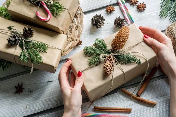 Közelkép a nő kezét díszítő karácsonyi ajándék doboz, papír barna levelek, a candy cane és a fenyő ágak, holiday koncepció — Stock Fotó