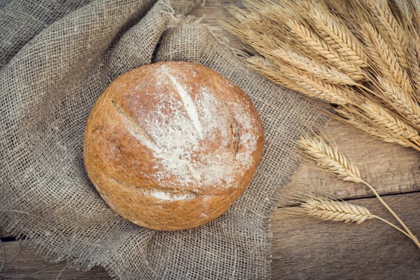 Круглый хлеб и пшеничные уши на мешковине — стоковое фото