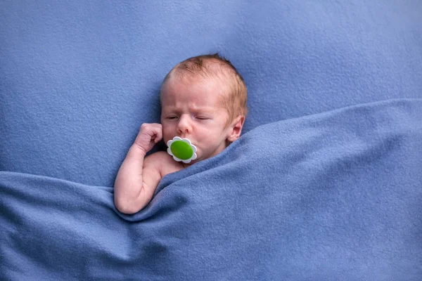 Nouveau-né garçon au lit dormant sous une couverture tricotée bleue Images De Stock Libres De Droits