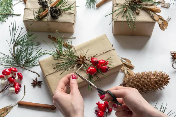 Mains de femme décorant des cadeaux de Noël avec corde, branches de pin et bâtons de cannelle, vue d'en haut Images De Stock Libres De Droits