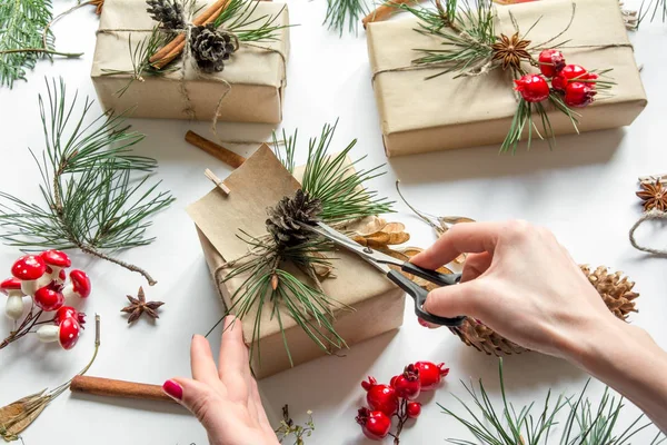 Woman's hands decorating gift boxes with empty card, cinnamon sticks, pine tree branches and cones, view from above — Stock Photo, Image