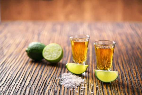 Dois tiros de tequila de ouro em um fundo de madeira marrom, selectiv — Fotografia de Stock