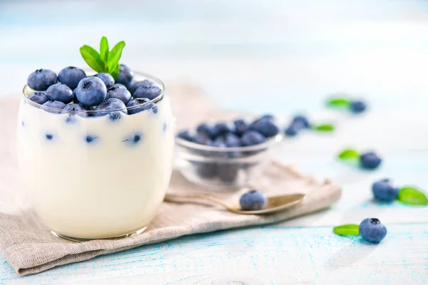 Clear jar of yogurt with blueberries over on wooden background — Stock Photo, Image