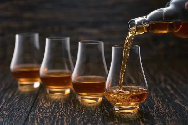 Man pouring whiskey in glasses on a wooden table selective focus — 스톡 사진