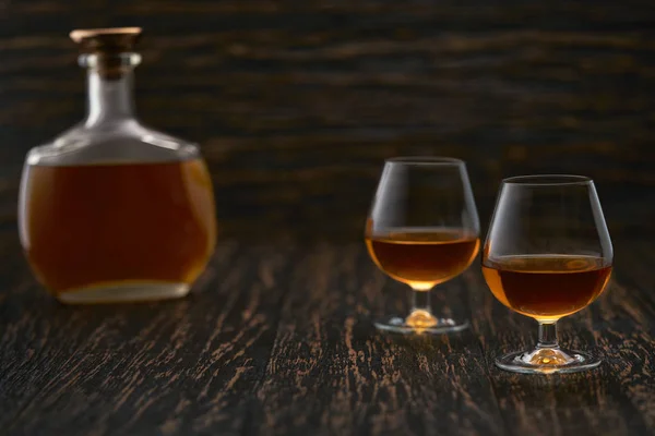 Two glasses of brandy or cognac and bottle on a wooden table. — 스톡 사진