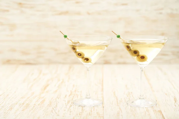 Dos cócteles de martini con aceitunas verdes sobre una mesa de madera . — Foto de Stock