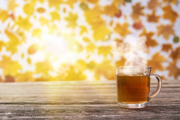 Transparente Glas-Tasse mit heißem Tee auf dunklem Holztisch, Herbst — Stockfoto