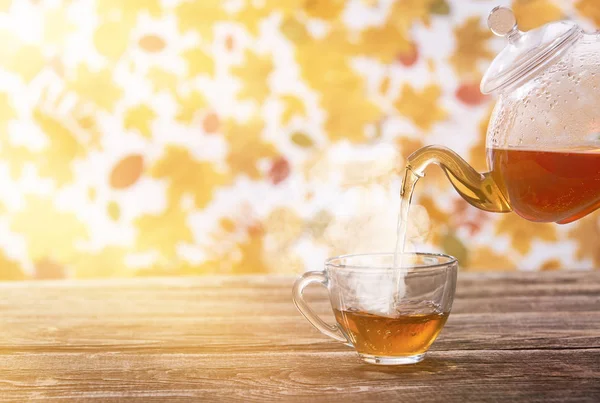 Tee wird in eine Glasschale auf dunklem Holztisch gegossen, Herbst zurück — Stockfoto