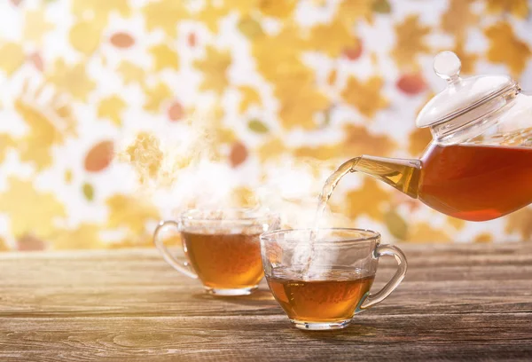 Čaj se nalévá do skleněného kelímku na tmavém dřevěném stole, podzim zpět — Stock fotografie