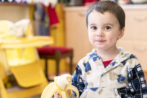 Lustige junge 2 jahre alt mit banane auf küche hintergrund — Stockfoto