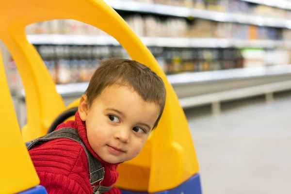 Малыш смотрит из корзины для детей в супермаркете на фоне полок с едой — стоковое фото