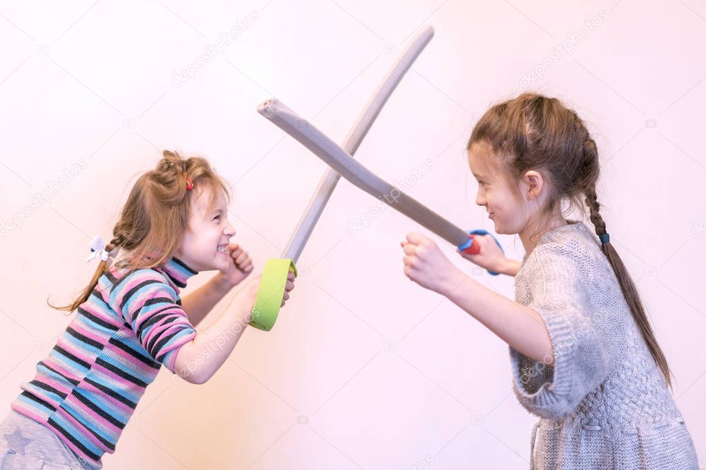 Two girls with toy swords play knights. Children's emotions.