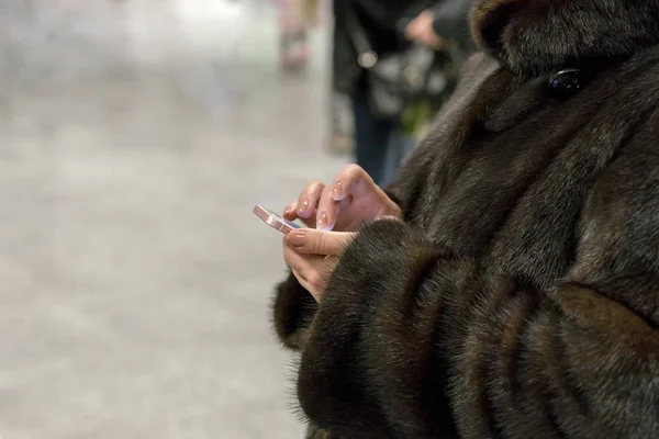Woman in a fur coat using a smartphone. — Stock Photo, Image