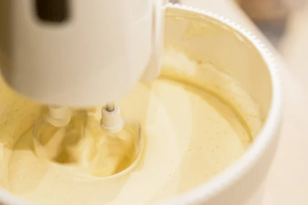 Un mixer da cucina con tuorli d'uovo gialli mescolati con zucchero in una cucina moderna. Girato ad angolo con la frusta miscelatore chiaramente visibile — Foto Stock