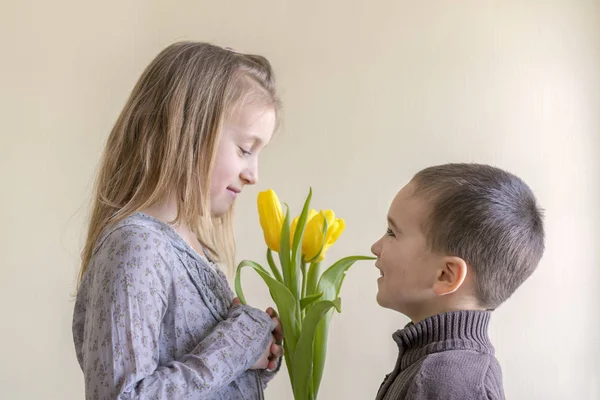 the little gentleman gives the girl a bunch of flowers. The little boy gives a bouquet of yellow tulips.