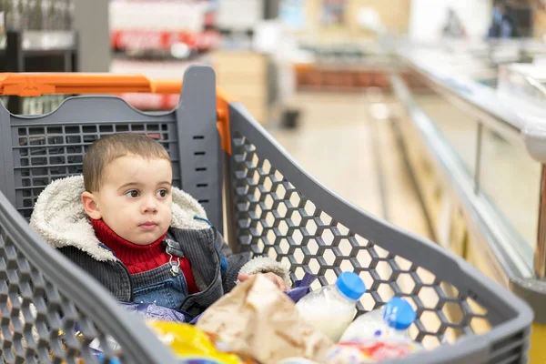 Carrinho cheio com comida no supermercado. No carrinho senta-se um bebê — Fotografia de Stock