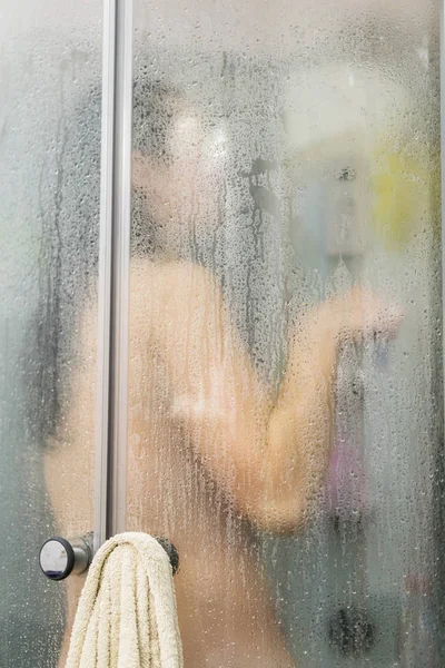 Красивая женщина в душе за стеклянной дверью с каплями. Женщине нравится принимать душ в ванной. Концепция ухода за телом и кожей — стоковое фото
