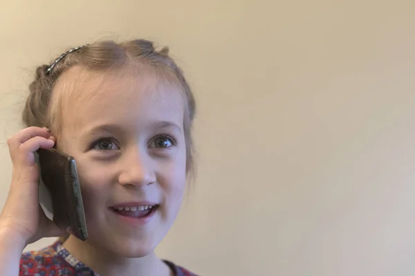 Menina bonito está falando no telefone celular e sorrindo. Menina falando no smartphone. Criança usando smartphone. Smartphone na mão . — Fotografia de Stock