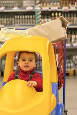 Yürümeye başlayan çocuk ters bir alışveriş merkezinde bir bebek arabası içinde alkol ile şişe