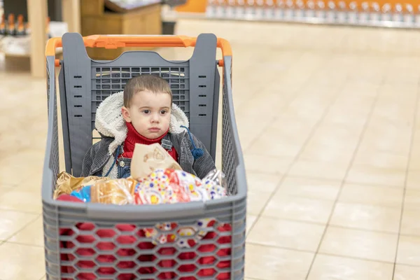 Хлопчик 2 роки в супермаркеті, сидить у кошику з різними продуктами — стокове фото