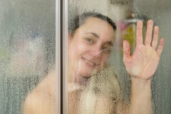 Mujer joven en la cabina de ducha agitando su mano — Foto de Stock