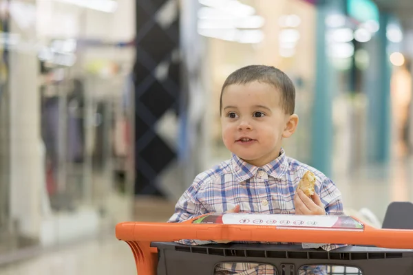 Menino monta em um carrinho através de um centro comercial . — Fotografia de Stock